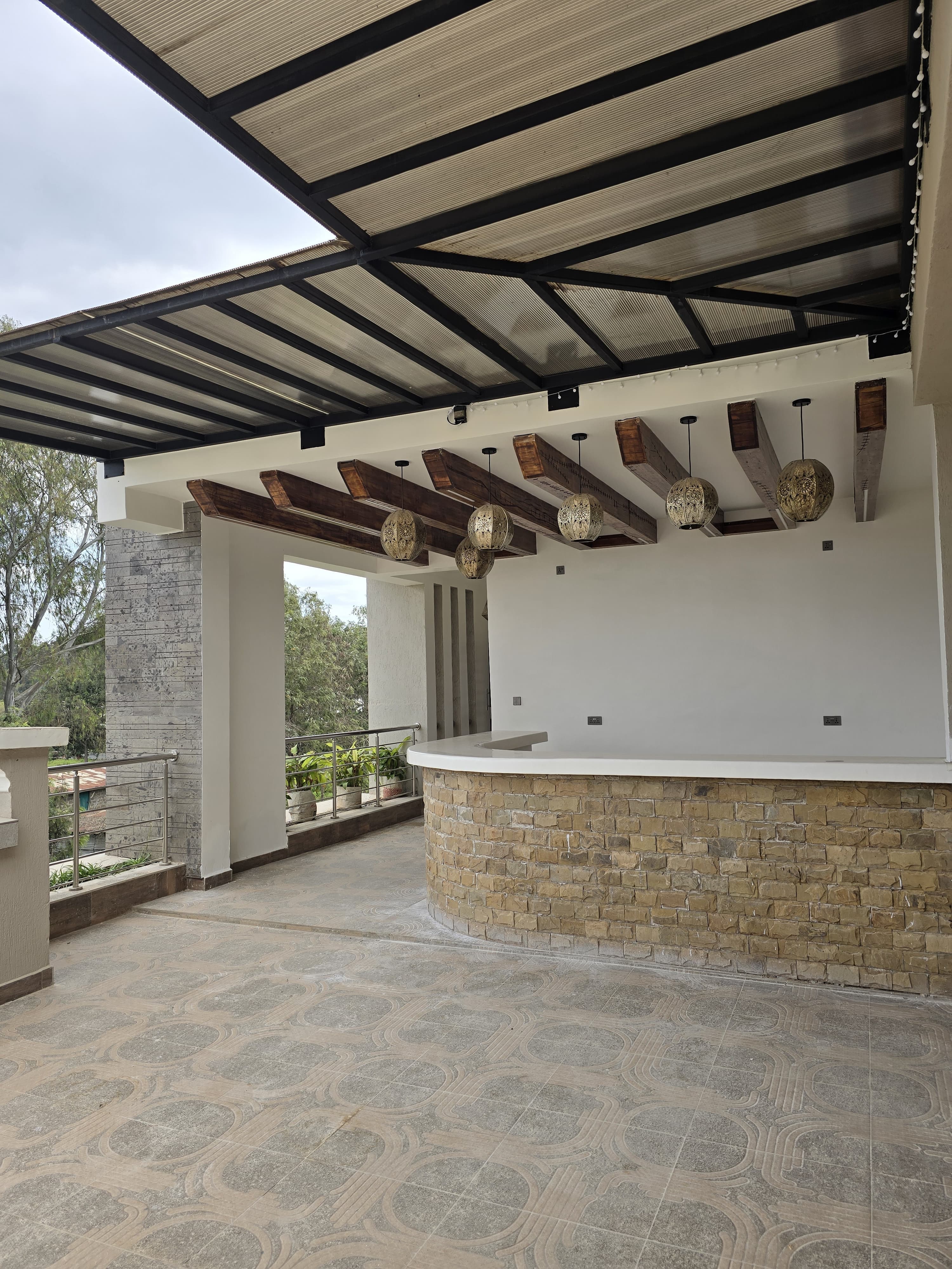 A covered entertainment terrace with black steel, timber beams and a stone-clad bar