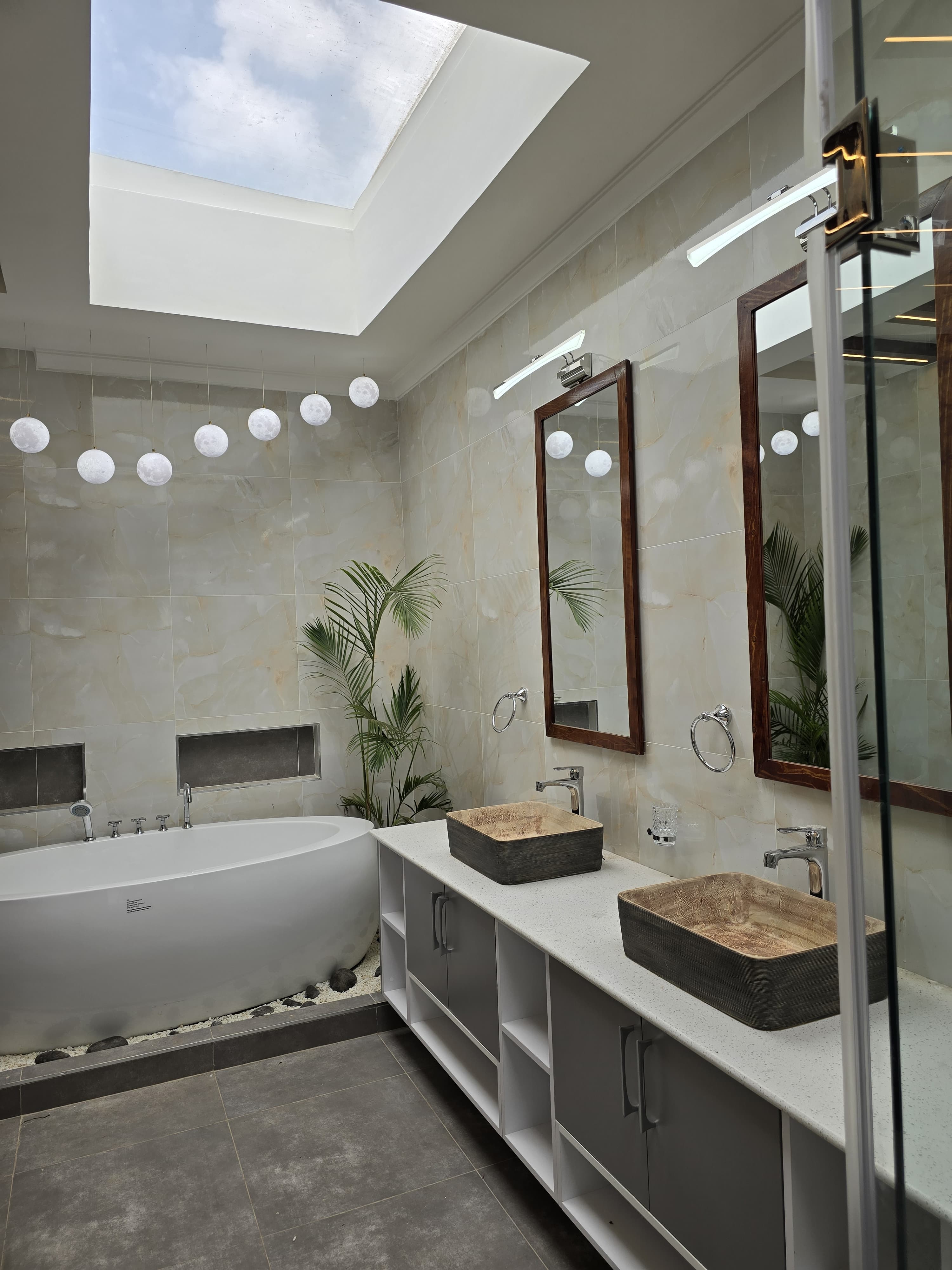 A skylit bathroom with double vanity, timber-framed mirrors and warm stone finishes