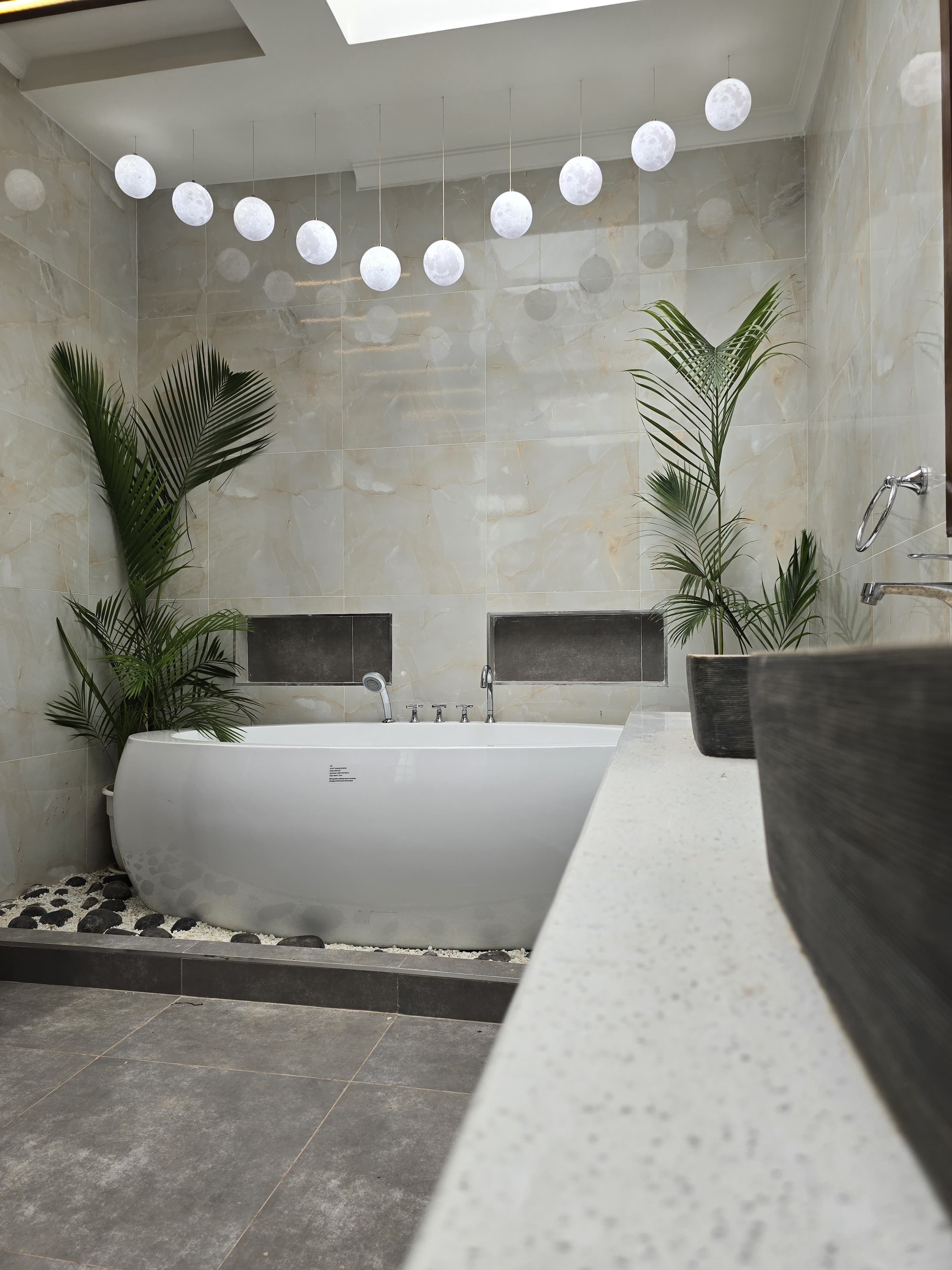 A freestanding bath framed by palms, stone finishes and sculptural pendant lights